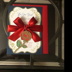 a card with a red ribbon on it and a rose attached to the front of it