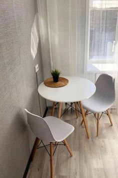 two white chairs and a table with a plant on it in front of a window