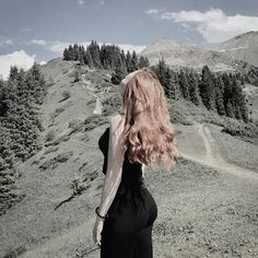 a woman standing on top of a lush green hillside next to a tree covered mountain