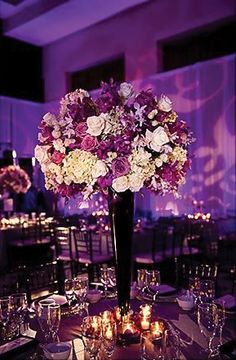 a tall vase filled with lots of flowers on top of a table covered in candles