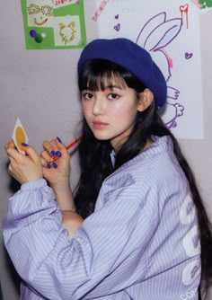 a young woman with long black hair wearing a blue hat and holding a pencil in her right hand