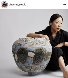 a woman sitting on the ground next to a large vase