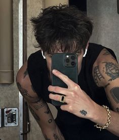 a man taking a selfie with his cell phone in front of him and tattoos on his arms