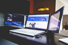 two computer monitors sitting next to each other on top of a wooden desk in front of a yellow car