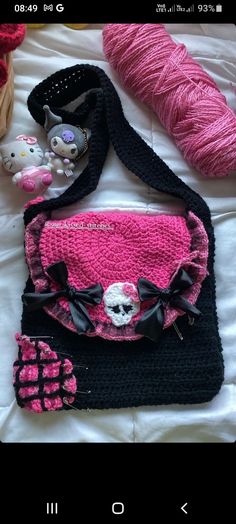 a pink and black handbag sitting on top of a bed next to a ball of yarn