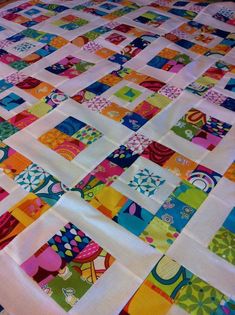 a colorful quilt is laying on top of a tablecloth that has many different colored squares in it