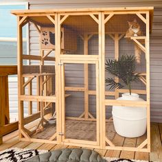 a large wooden bird cage on the outside of a house next to a potted plant