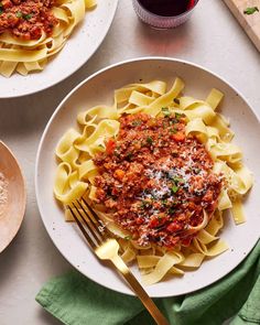 two plates of pasta with meat sauce and parmesan cheese on the side next to a glass of wine