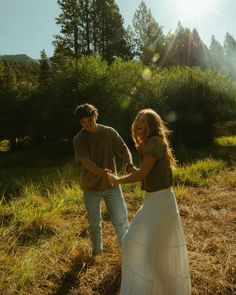 a man and woman standing in the grass holding each other's hands with trees in the background