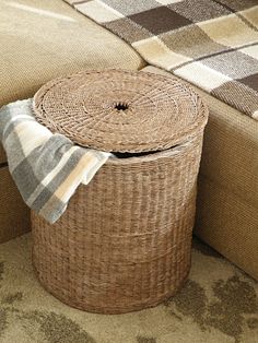 a brown basket sitting on top of a couch next to a plaid tablecloth covered ottoman