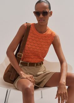 a woman sitting on top of a white chair wearing an orange shirt and khaki shorts