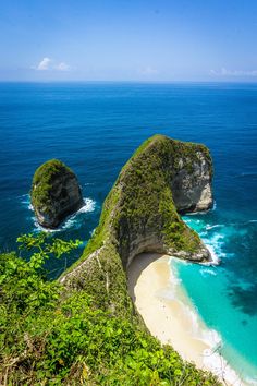 two large rocks sitting on top of a lush green hillside next to the ocean with blue water