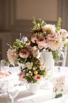 a vase filled with lots of flowers on top of a table next to wine glasses