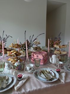 the table is set with pink and white desserts, silverware, and candles