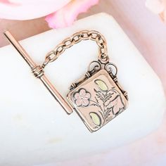 Beautiful square Victorian locket with T bar chain. The locket features pink gold flowers in the front with green gold leaves. It hangs on a 1.5 inch length of chain with a T bar at the opposite end. Includes the original frames and photo covers inside. Pics 7&8 show it with an optional added ring to function as a bail from which to hang the piece, so it would dangle as two pieces. The locket bears the mark of S.K. Merrill and Co of Providence, Rhode Island - in business from 1871 to 1915. Fits Antique Rose Gold Jewelry With Charms, Engraved Rose Gold Square Pendant Jewelry, Antique Square Locket Pendant Jewelry, Vintage Charm Jewelry Gift With Rectangular Shape, Vintage Charm Rectangular Jewelry Gift, Antique Jewelry Gift With Box Clasp, Antique Square Pendant Locket Jewelry, Antique Rose Gold Jewelry For Keepsake, Rectangular Vintage Charm Jewelry Gift