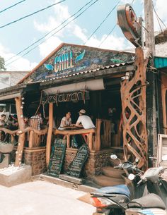 people are sitting at the outside bar of a small restaurant in an old town with graffiti written on it