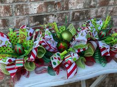 a white table topped with green and red christmas bowes next to a brick wall