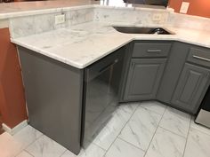 an empty kitchen with marble counter tops and gray cabinets in the corner, next to a dishwasher