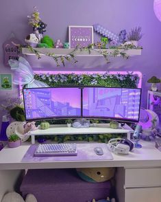 a desk with two computer monitors and a keyboard on it in front of a purple wall