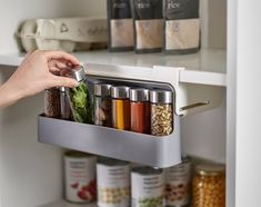 a person picking up food from the bottom shelf in a pantry with spices and seasonings