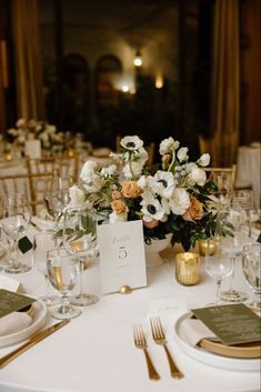 the table is set with white and gold place settings, silverware, and flowers