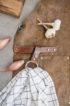 an open brown leather bag with garlic on the floor next to it and other items