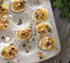 an overhead view of several deviled eggs with toppings on a baking tray next to parsley