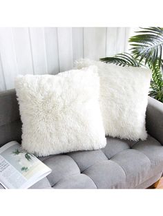 two white pillows sitting on top of a gray couch next to a book and potted plant