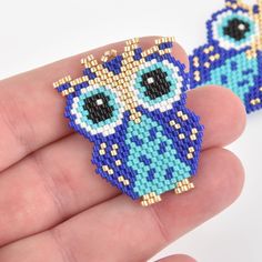 a hand holding two small beaded owls on it's fingers, one is blue and the other is yellow