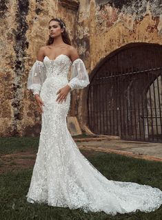 a woman standing in front of an old building wearing a wedding dress with sheer sleeves