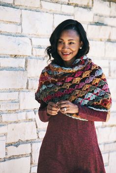 a woman standing in front of a brick wall wearing a crocheted shawl