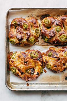 four pizzas on a baking sheet with cheese and jalapenos in them