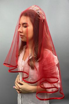 a woman wearing a red veil and holding a cell phone in her right hand while standing against a gray background