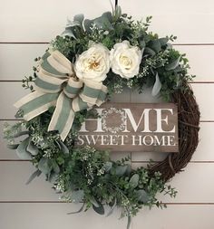 a wreath with white roses and greenery is hung on the wall next to a sign that says home sweet home