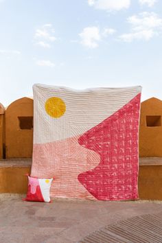 a large blanket sitting on top of a cement wall next to a pillow and pillows