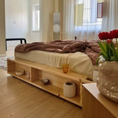 a bed sitting on top of a wooden floor next to a vase filled with flowers