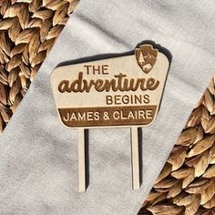 a wooden sign that says the adventure begins on it's side and leaves surrounding it