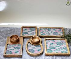 four square wooden trays with painted leaves on them, one is holding a bowl and the other two are serving dishes