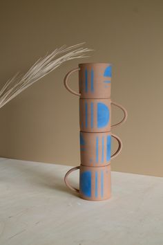 a stack of three vases sitting on top of a table next to a plant