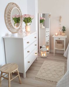 a bedroom with white furniture and flowers in vases on the dresser next to it