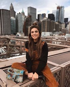 a woman sitting on top of a bridge next to a city filled with tall buildings