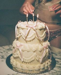 a woman lighting candles on top of a cake with pink ribbons and bows around it