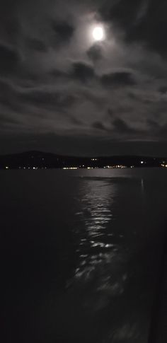 the moon shines brightly in the dark night sky over the water and hills on the horizon