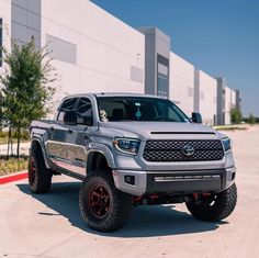 a silver truck is parked in front of a building with red rims and tires