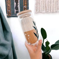 a hand holding a glass with a design on it next to a potted plant