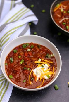 two bowls filled with chili and cheese on top of a table next to each other