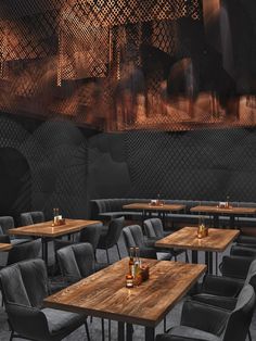 an empty restaurant with wooden tables and grey velvet chairs, along with bottles of alcohol