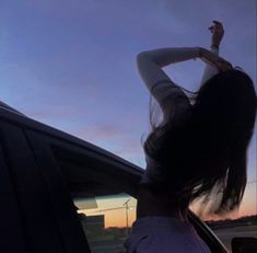 a woman leaning out the window of a car with her hand up in the air