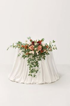 an arrangement of flowers and greenery on top of a white cloth covered tablecloth