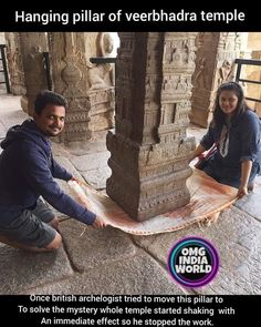 two people sitting on the ground next to a stone pillar with an advertisement about hanging pillar of veerhada temple